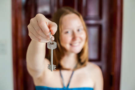 A female hand holding a key to the house on a background of a wooden door. Owning real estate concept.の写真素材