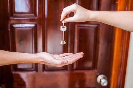 Female hand giving a key to the house a man's hand on a background of a wooden door. Owning real estate concept.の写真素材