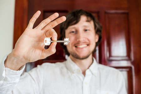 Men's hands hold house key on a background of a wooden door. Owning real estate concept.の写真素材