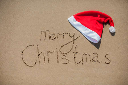 inscription on the wet sand and cap of Santa Claus Christmas in tropical climate conceptの写真素材