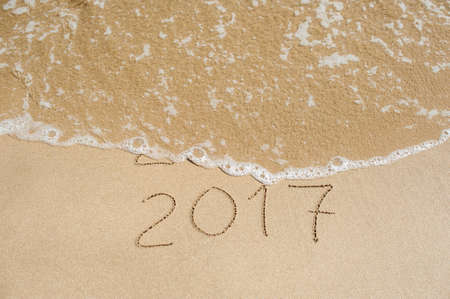 New Year 2017 is coming concept - inscription 2016 and 2017 on a beach sand, the wave is almost covering the digits 2016.の写真素材