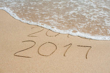New Year 2017 is coming concept - inscription 2016 and 2017 on a beach sand, the wave is almost...