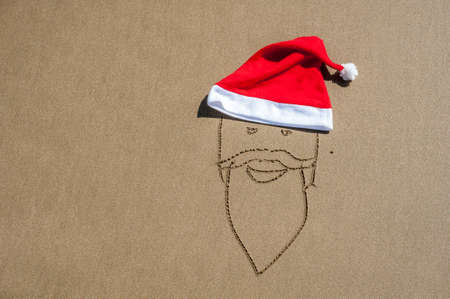The image of Santa Claus on the sand and a red Santa's hat.の写真素材
