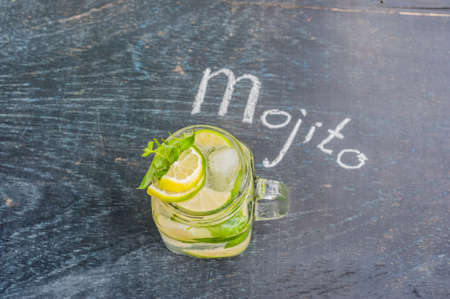 glass of mojito with lime and mint ice cube close-up on dark wood background. The inscription in chalk MOJITOの写真素材