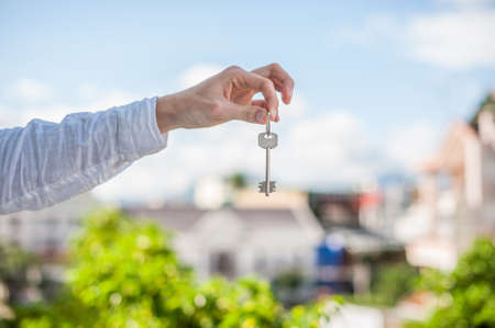 A man holding a key to the house on a background of houses in the city. Deal with the real estate concept.の写真素材