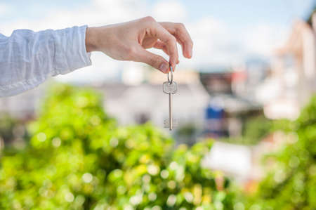 A man holding a key to the house on a background of houses in the city. Deal with the real estate concept.の写真素材