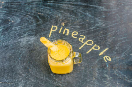Pineapple cocktail with a slice of pineapple on a wooden background and inscription in chalk pineapple. Tropical cocktail concept.の写真素材