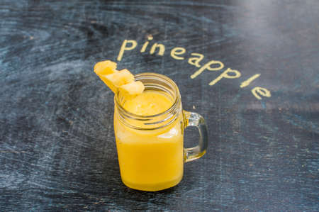 Pineapple cocktail with a slice of pineapple on a wooden background and inscription in chalk pineapple. Tropical cocktail concept.の写真素材