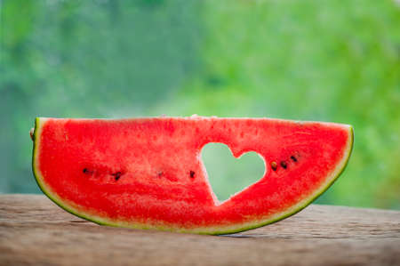 Piece of watermelon with heart at the backdrop of greenery. Space for text. Flat lay composition. love concept. Valentine's Day Conceptの写真素材