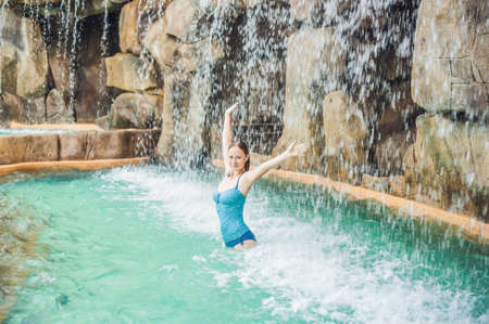 Young woman relaxing under a waterfall in aquapark. Vacation conceptの写真素材
