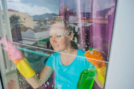 Beautiful female maid doing the housework while using a spray, washing windows. cleaning company conceptの写真素材