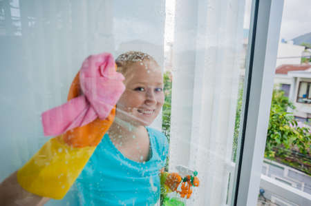 Beautiful female maid doing the housework while using a spray, washing windows. cleaning company...