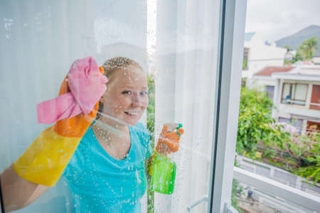 Beautiful female maid doing the housework while using a spray, washing windows. cleaning company conceptの写真素材