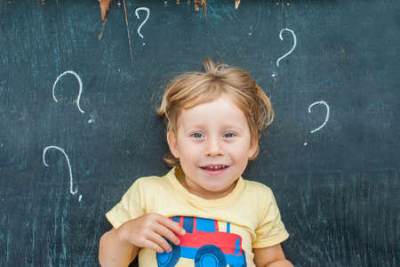 Top view of a little blond kid boy with question mark on blackboard. Concept for confusion, brainstorming and choice.の写真素材