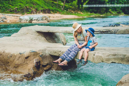 Mom and young son sitting on bridge on a background of the river. Travelling with kids conceptの写真素材