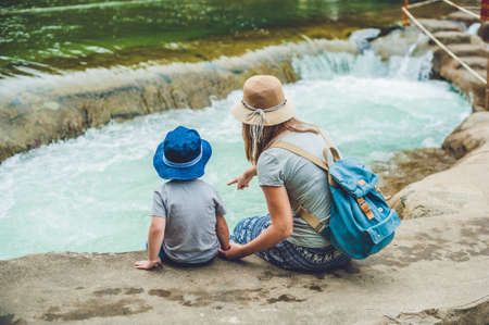 Mom and young son sitting on bridge on a background of the river. Travelling with kids conceptの写真素材