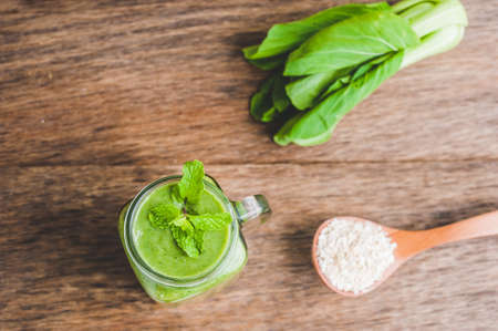 Mason jar mugs filled with green spinach, banana and coconut milk health smoothie with with a spoon of oatmeal on wooden rustic table. Green healthy food conceptの写真素材