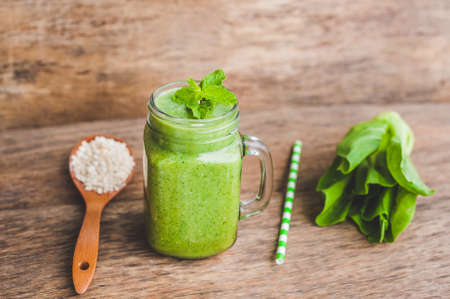 Mason jar mugs filled with green spinach, banana and coconut milk health smoothie with with a spoon of oatmeal on wooden rustic table. Green healthy food conceptの写真素材