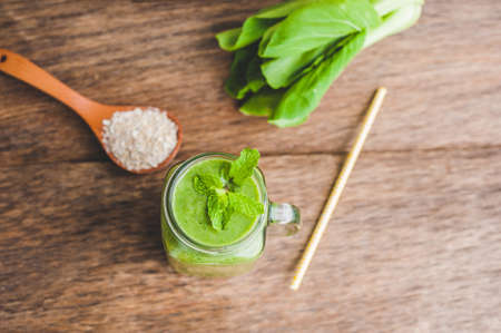 Mason jar mugs filled with green spinach, banana and coconut milk health smoothie with with a spoon of oatmeal on wooden rustic table. Green healthy food conceptの写真素材