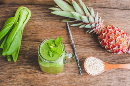 Mason jar mugs filled with green spinach, banana and coconut milk health smoothie with with a spoon of oatmeal on wooden rustic table. Green healthy food conceptの写真素材