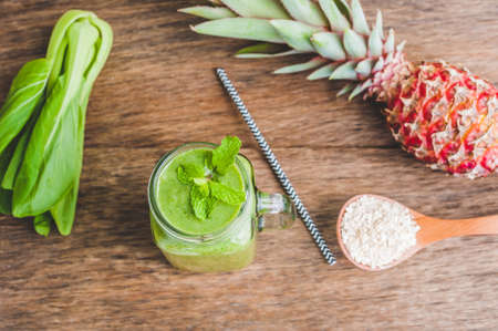 Mason jar mugs filled with green spinach, banana and coconut milk health smoothie with with a spoon of oatmeal on wooden rustic table. Green healthy food conceptの写真素材