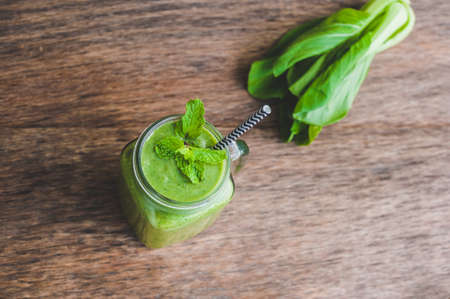 Mason jar mugs filled with green spinach, banana and coconut milk health smoothie with with a spoon of oatmeal on wooden rustic table. Green healthy food conceptの写真素材