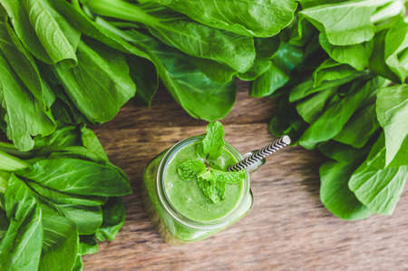 Mason jar mugs filled with green spinach, banana and coconut milk health smoothie with with a spoon of oatmeal on wooden rustic table. Green healthy food conceptの写真素材