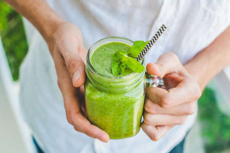 Mason jar mugs filled with green spinach, banana and coconut milk health smoothie with with a spoon of oatmeal In hands on wooden rustic table. Green healthy food conceptの写真素材