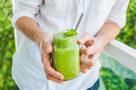 Mason jar mugs filled with green spinach, banana and coconut milk health smoothie with with a spoon of oatmeal In hands on wooden rustic table. Green healthy food conceptの写真素材