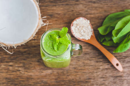Mason jar mugs filled with green spinach, banana and coconut milk health smoothie with with a spoon of oatmeal on wooden rustic table. Green healthy food conceptの写真素材