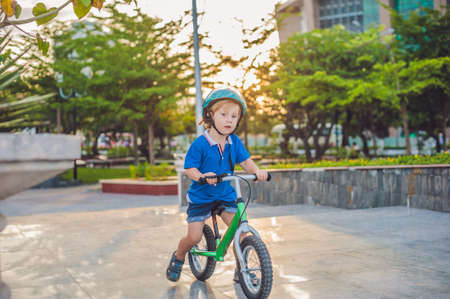 Active blond kid boy driving bicycle in the park near the sea. Toddler child dreaming and having fun on warm summer day. outdoors games for children. Balance bike conceptの写真素材