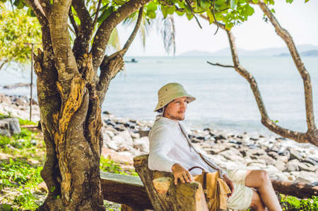 Tourist resting on a bench under a tree by the sea. Vintage toned photo.の写真素材