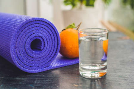 Yoga mat, water, orange and mango on a wooden background. Equipment for yoga. Concept healthy lifestyle, diet and sport. Copy space. Selective focus.の写真素材