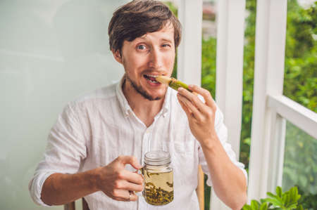 Cane sugar concept. The man jokingly eating sugar cane and drinks tea.