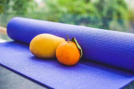 Yoga mat, water, orange and mango on a wooden background. Equipment for yoga. Concept healthy lifestyle, diet and sport. Copy space. Selective focus.の写真素材