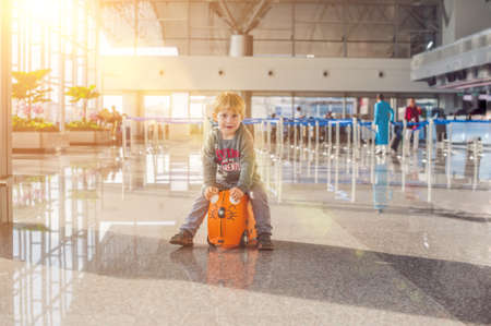 Cute little boy with orange suitcase at airport.の写真素材