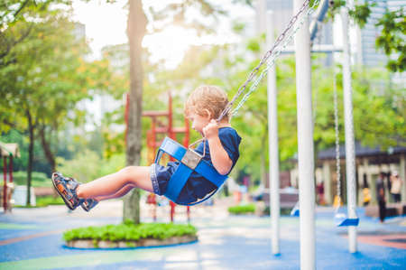 Lovely blond little boy on a swing in the park. Adorable boy having fun at the playground.の写真素材