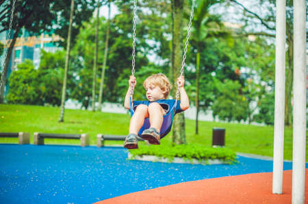 Lovely blond little boy on a swing in the park. Adorable boy having fun at the playground.の写真素材