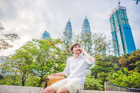 Young Man on the phone. Dressing in a white shirt, beige shorts. Young handsome businessman in casual clothes is sitting outside a business district, making a call on a mobile phone. Mobile Office concept.の写真素材