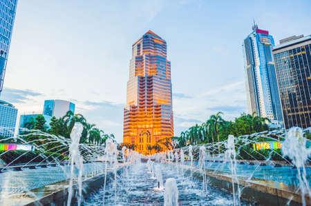 Skyscraper lit with yellow light on the background of a fountain.の写真素材