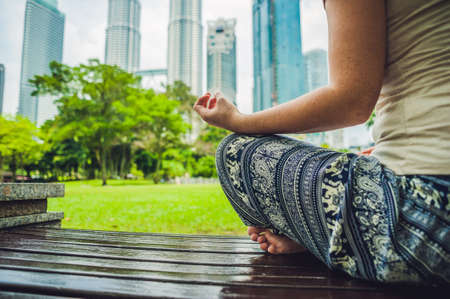 Young woman meditating in the park on the background of skyscrapers.の写真素材
