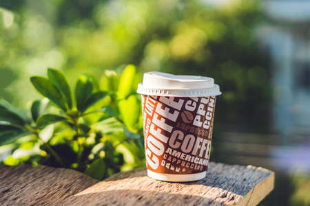 A paper cup with coffee on an old wooden background.