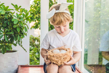 Cute little child boy wearing bunny ears on Easter day. Boy holding nest with eggs.の写真素材