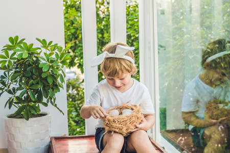 Cute little child boy wearing bunny ears on Easter day. Boy holding nest with eggs.