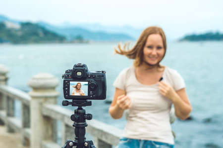 A young woman blogger leads her video blog in front of a camera by the sea.