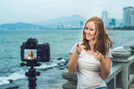 A young woman blogger leads her video blog in front of a camera by the sea.の写真素材