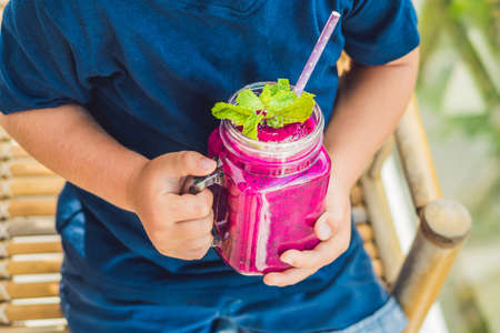 The boy holds smoothies from a dragon fruit with a mint leaf and a drinking straw.の写真素材