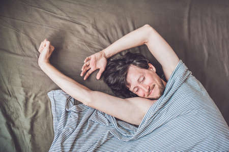 Beautiful young man lying down in bed and sleeping, top view. Do not get enough sleep concept.の写真素材