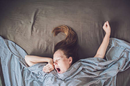 Beautiful young woman lying down in bed and sleeping, top view. Do not get enough sleep concept.