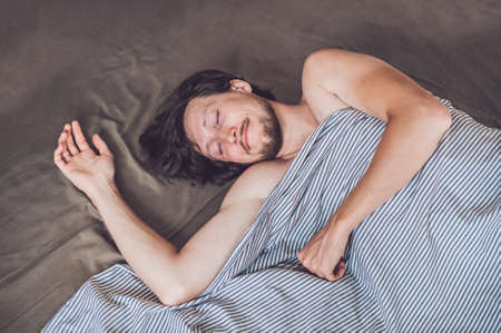 Beautiful young man lying down in bed and sleeping, top view. Do not get enough sleep concept.の写真素材